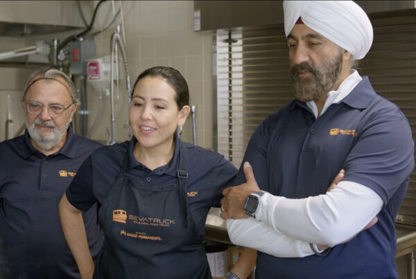 Three food truck team members, including a woman and two men, are engaged in a discussion in a kitchen.