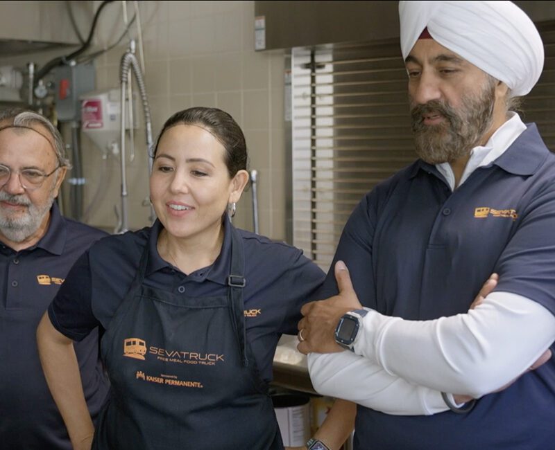 Three food truck team members, including a woman and two men, are engaged in a discussion in a kitchen.