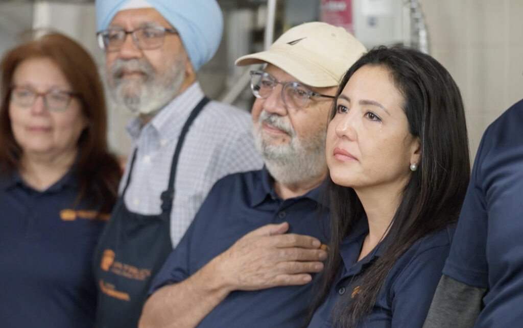 A diverse group of people, including a woman with long black hair, stands attentively in a professional setting.