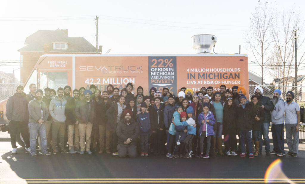 A large group of diverse people, including children, stands in front of a mobile food truck.