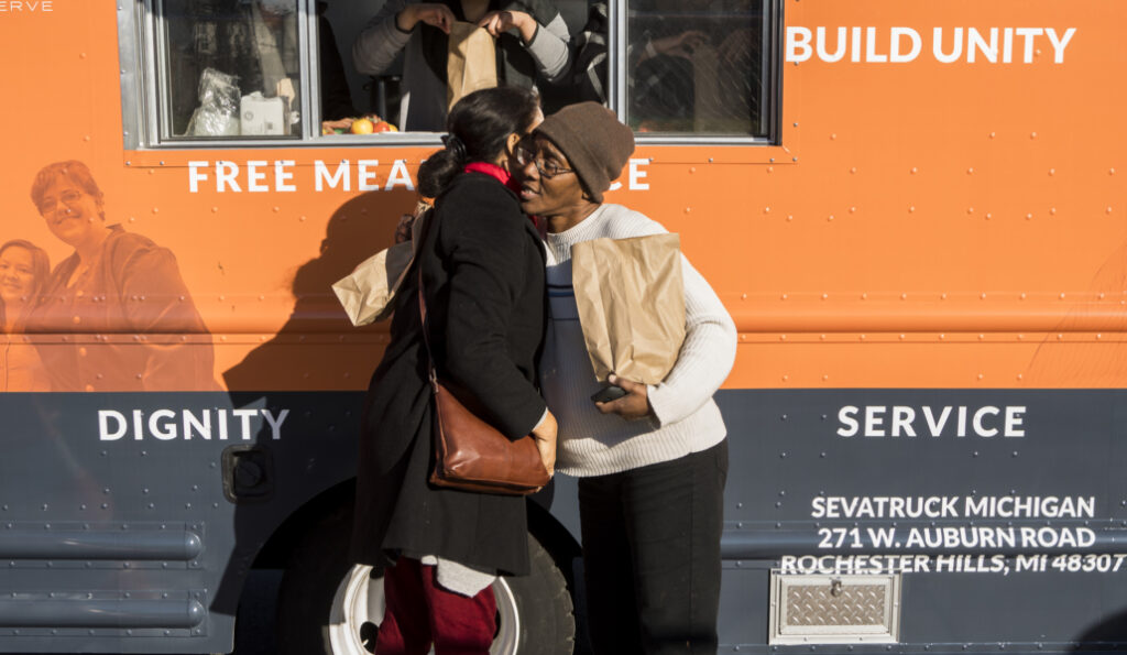 Two women share a hug in front of an orange service truck