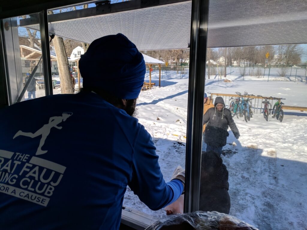 A person hands food through a window to a woman outside in snowy weather.