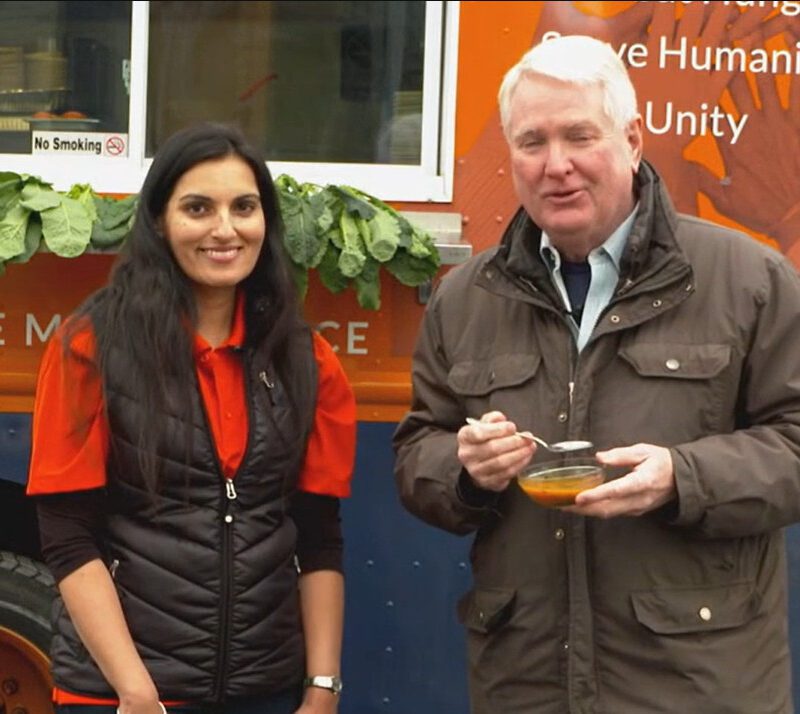 A woman and a man stand in front of food truck.