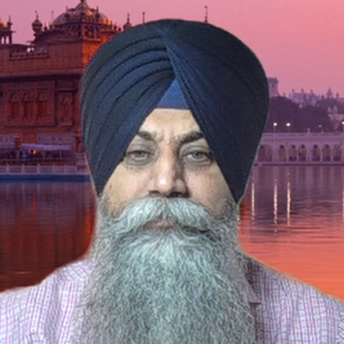 A man with a long white beard and a dark blue turban stands in front of a river and historic building at sunset.